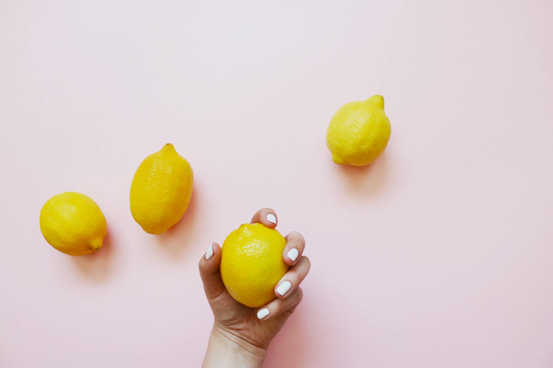 Hand holding a fresh lemon on a soft pink background, symbolizing the natural, intuitive design of lemon vibrators