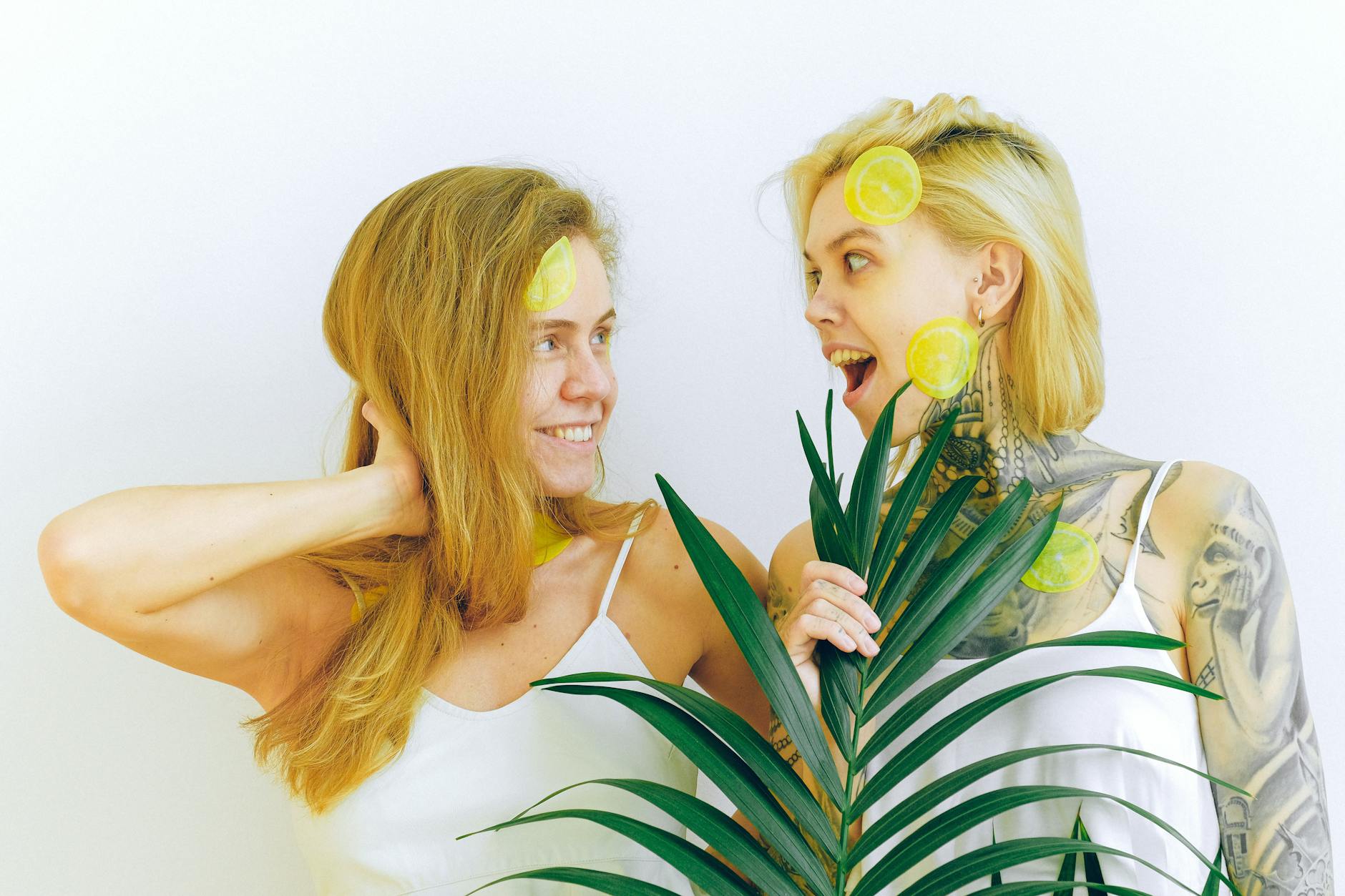 Two women smiling indoors, surrounded by plants and warm light, expressing comfort and authentic joy.