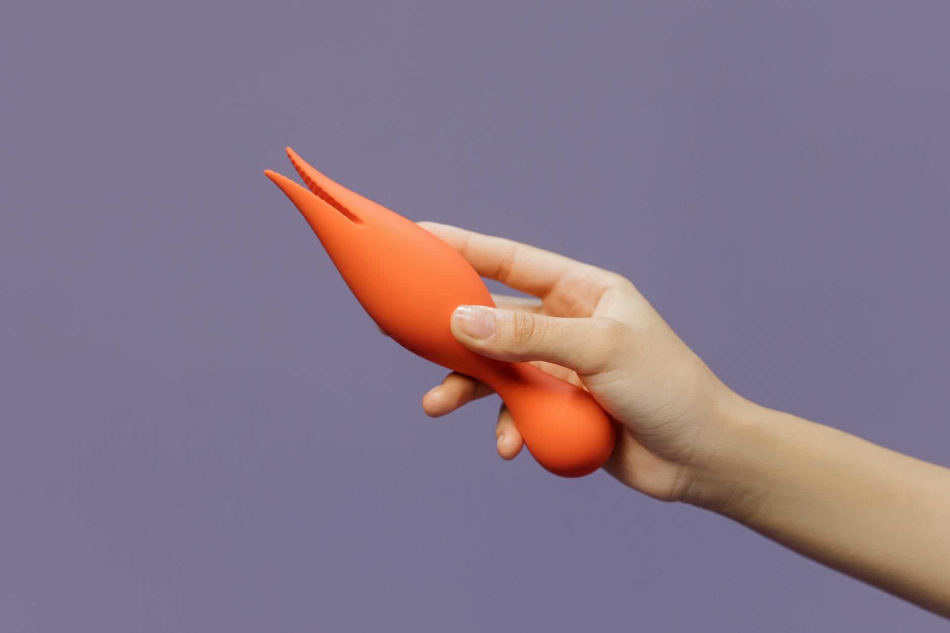 Hand holding a lemon clitoral vibrator against a minimalist purple backdrop.