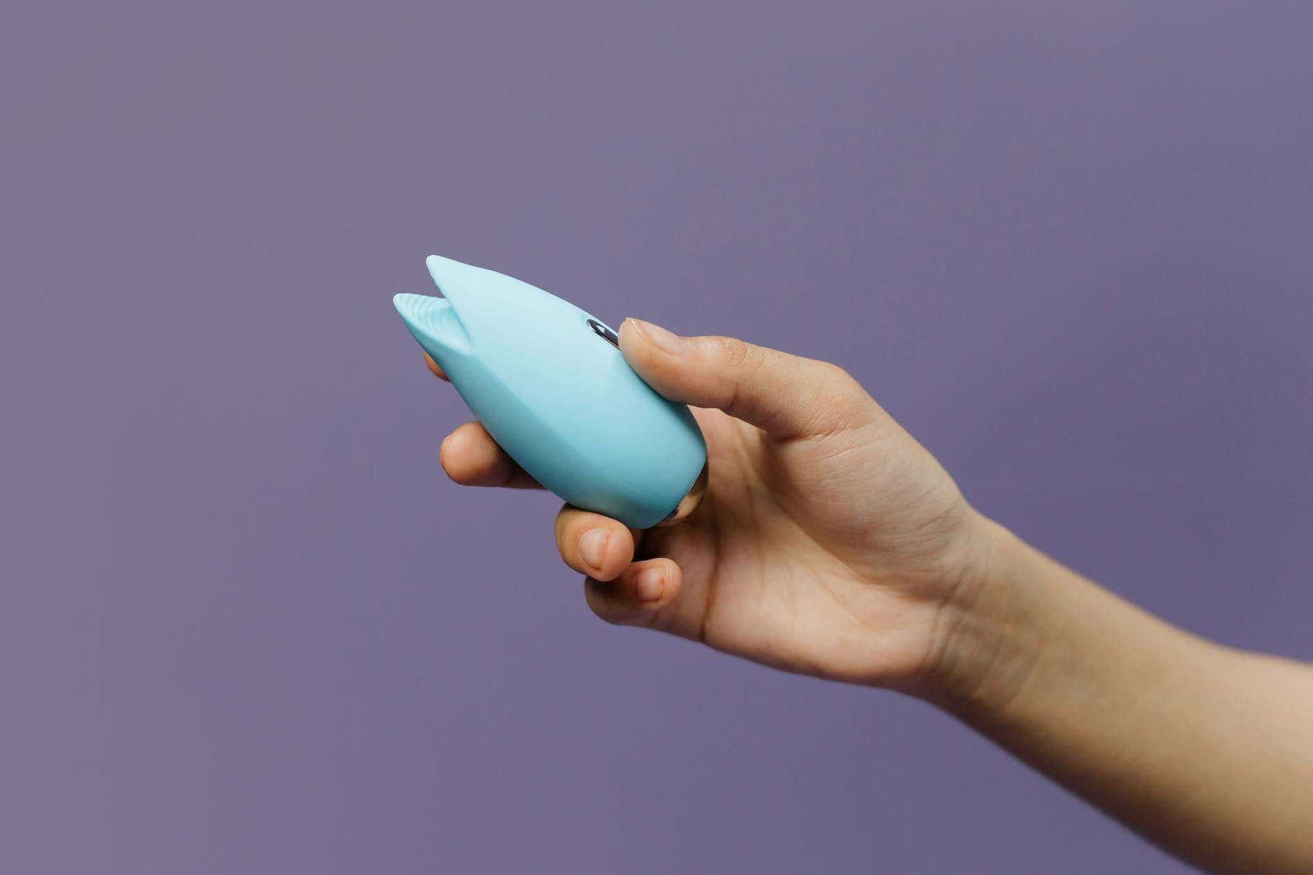 A lemon-colored silicone vibrator held in hand against a solid purple background, showing the design of modern clitoral toys.